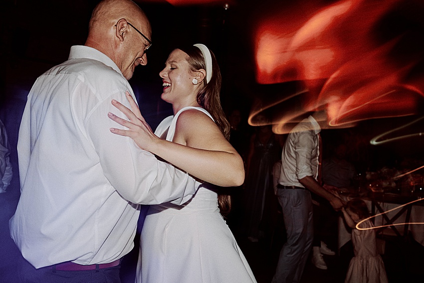 Ein Mann und eine Frau tanzen ausgelassen auf der Hochzeit Hannover. Die Frau trägt ein weißes Kleid und Stirnband, der Mann ein weißes Hemd. Verschwommene Lichter bilden eine dynamische Kulisse, die an festliche Feiern im eleganten Hotel Kaiserhof erinnert.